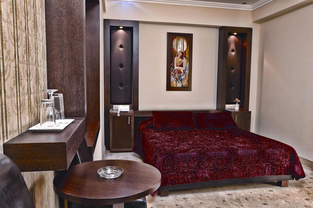 A hotel room with a large bed, a small round table, a nightstand, and a wall-mounted artwork.