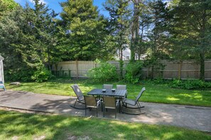 An outdoor patio with a table and chairs, surrounded by a wooden fence and lush greenery.