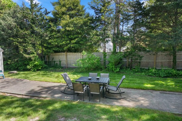 An outdoor patio with a table and chairs, surrounded by a wooden fence and lush greenery.