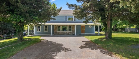A two-story house with a stone foundation, a covered porch, and a front yard with trees.