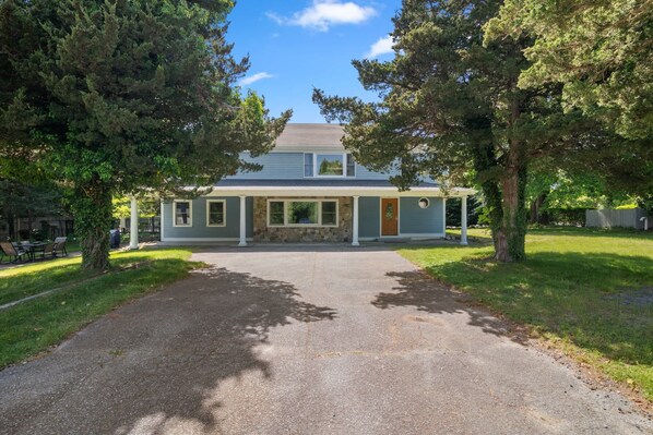 A two-story house with a stone foundation, a covered porch, and a front yard with trees.