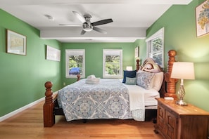 A bedroom with a bed, a nightstand, a dresser, a ceiling fan, and two windows.