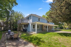 A two-story house with a covered porch, a deck, and a patio area with outdoor furniture.