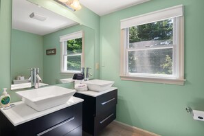 A bathroom with two white sinks, a mirror, and a window.