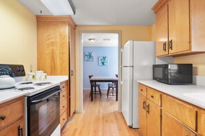 A kitchen with wooden cabinets, a stove, a microwave, and a refrigerator. There is a dining table with chairs in the background. - Mins to Nauset Beach & Walkable to Town! (Orleans)
