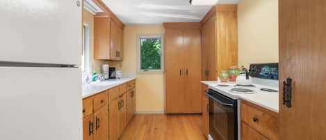 A kitchen with wooden cabinets, a white countertop, a stove, and a window with a view of greenery.