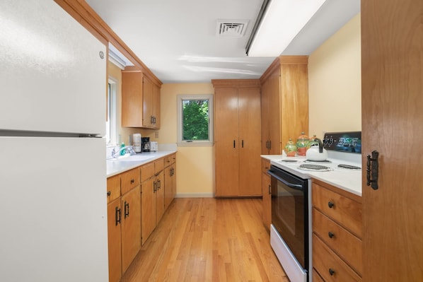 A kitchen with wooden cabinets, a white countertop, a stove, and a window with a view of greenery.