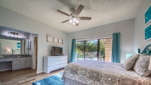 Un dormitorio con una cama grande, ventilador de techo, televisor, cómoda y vistas al exterior.