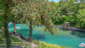 Un parque tranquilo a la orilla del río, con una pasarela de madera, un puente y una masa de agua azul cristalina.