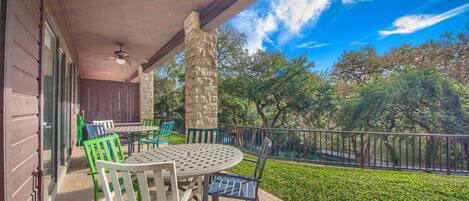 An outdoor patio with a round table and chairs, a stone pillar, and a view of trees and a fence.