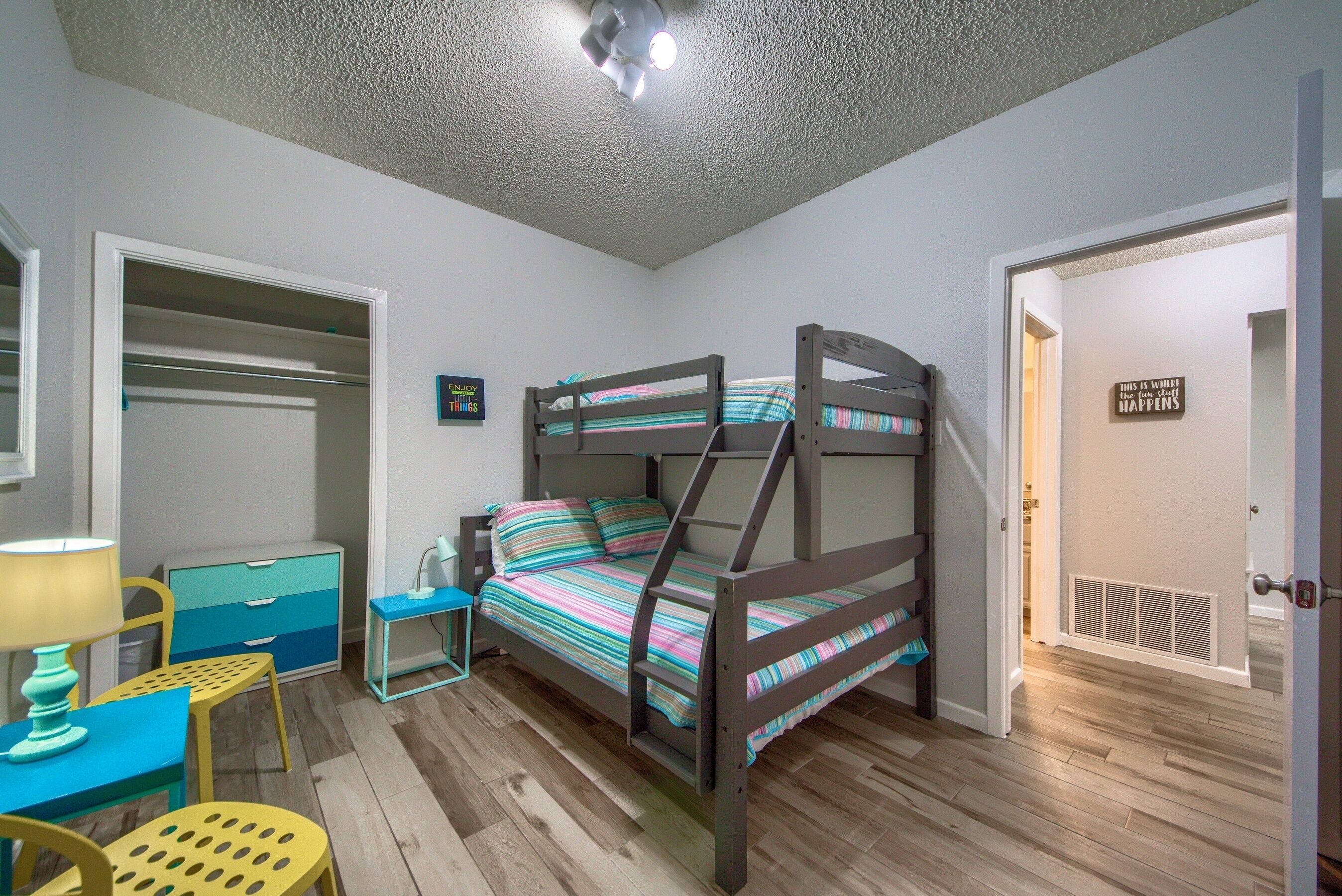 Une chambre avec un lit superposé, un bureau avec une lampe, une chaise et une armoire.