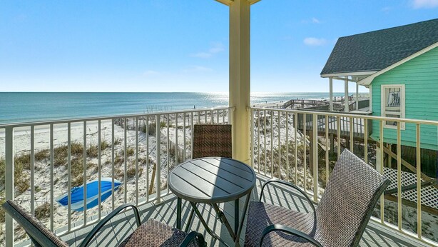 Un balcon avec vue sur la plage et l’océan, agrémenté de meubles en osier et d’une petite table.