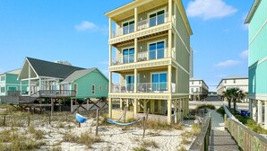 Un immeuble à plusieurs étages situé en bord de mer, doté de balcons, d’une terrasse en bois et d’une plage de sable.