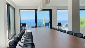 A conference room with a long table and chairs, large windows with a view of the sea, and modern pendant lighting. - Luxury villa Colomba in Brela, seafront (Brela)