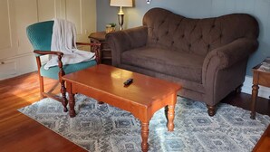 A living room with a brown sofa, a wooden coffee table, a teal armchair, and a patterned rug. - Located in the Historic downtown district, cozy studio, wifi. (Auburn)