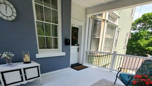 A covered porch with a white ceiling, a clock, a small table with candles, and two blue chairs. - Located in the Historic downtown district, cozy studio, wifi. (Auburn)