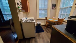 A compact kitchen with a gas stove, a small refrigerator, a dining table with chairs, and a window with blinds. - Located in the Historic downtown district, cozy studio, wifi. (Auburn)