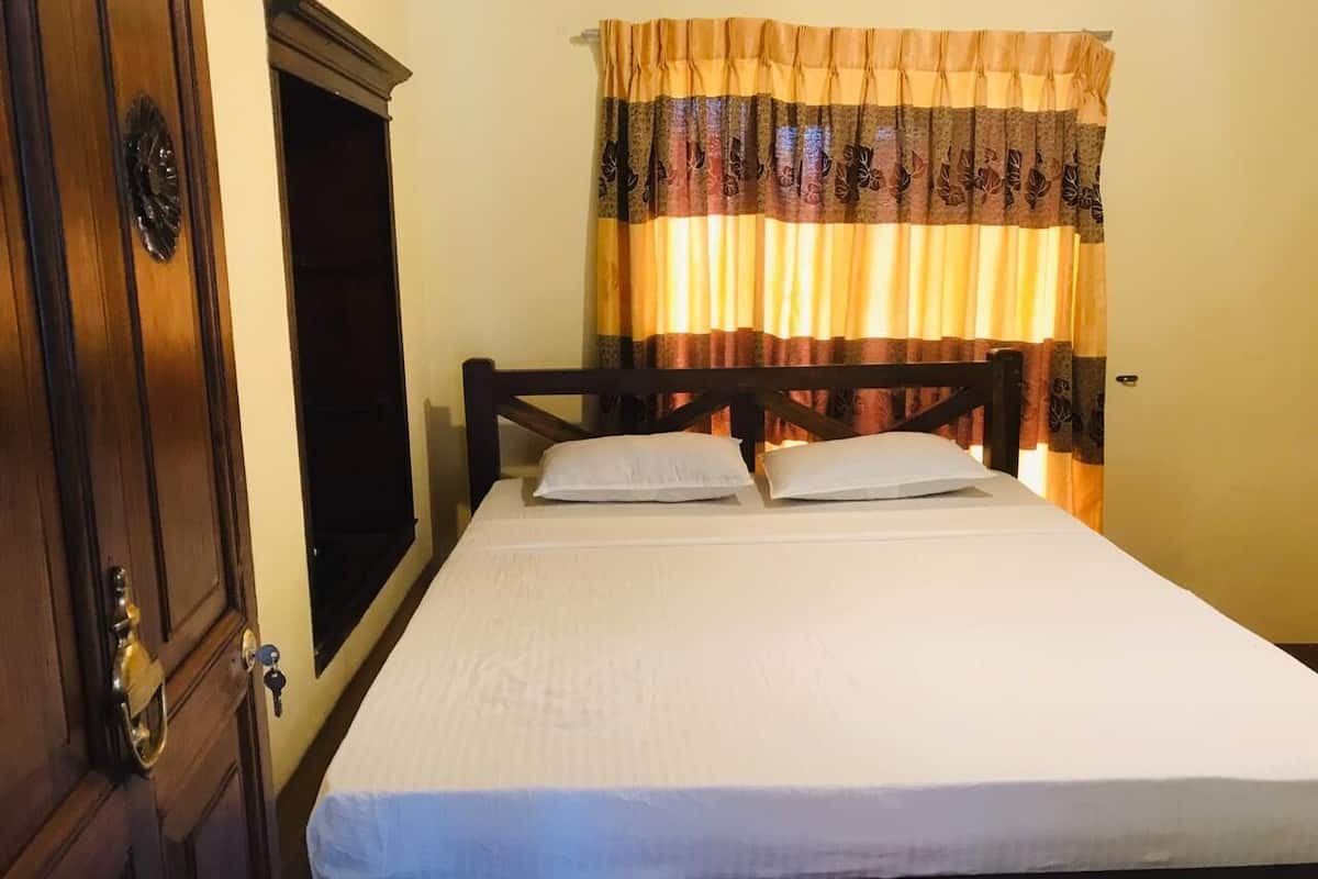 A bed with a white mattress and two pillows, a wooden headboard, a wooden wardrobe with a brass handle, and a window with a curtain.