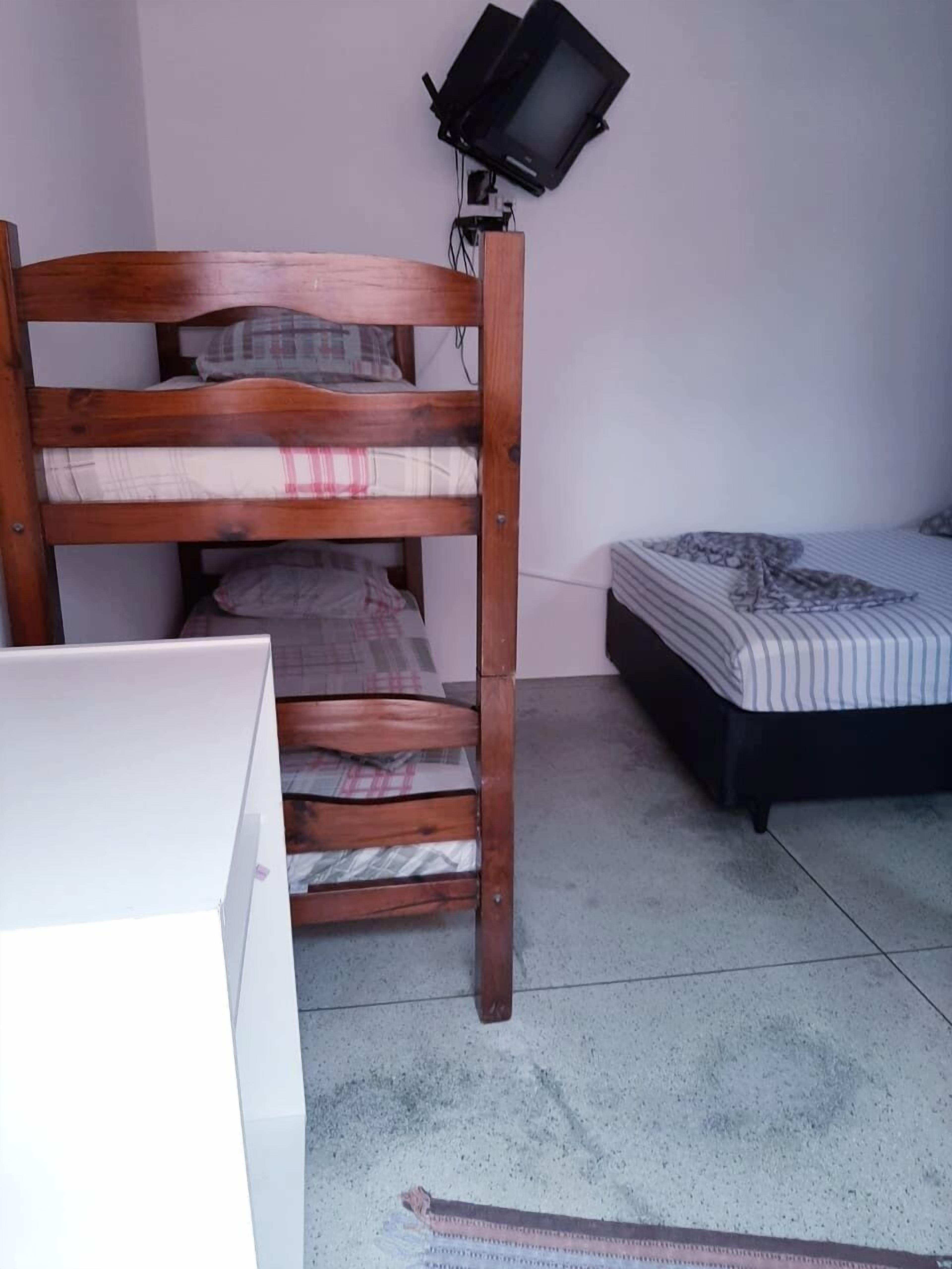 A bunk bed with a television on top, a small bed, and a white desk.
