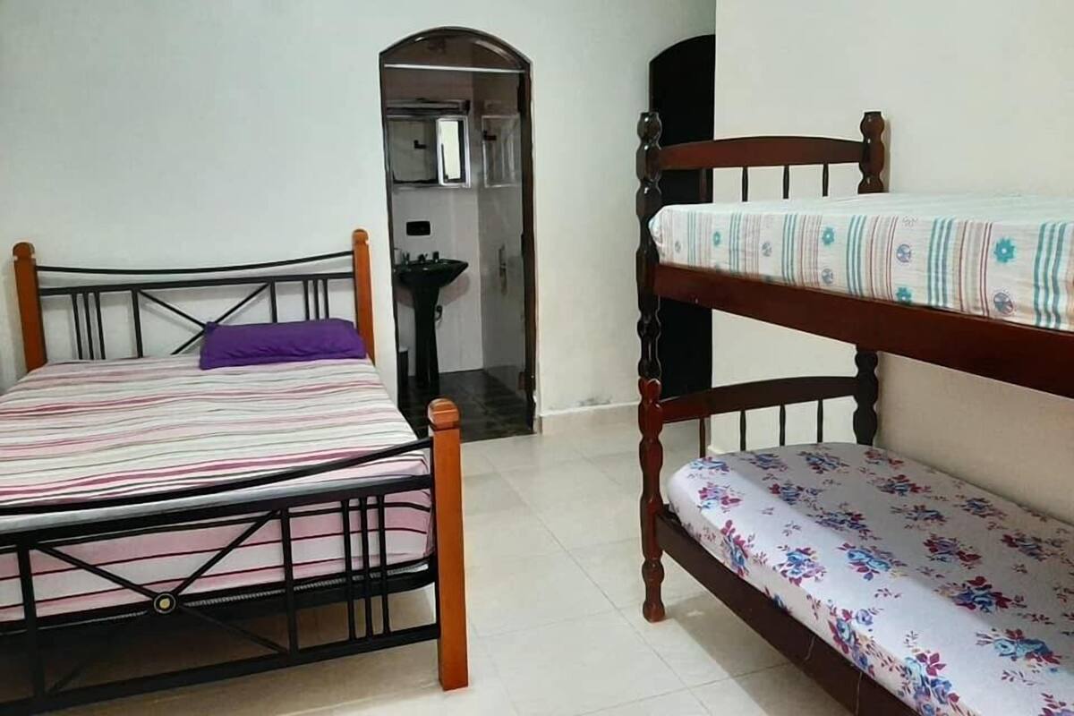 Una habitación con dos camas, una con una colcha a rayas y la otra con estampado floral. Hay un lavamanos y un espejo en una esquina.