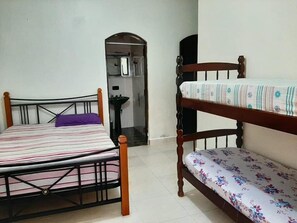 Una habitación con dos camas, una con una colcha a rayas y la otra con estampado floral. Hay un lavamanos y un espejo en una esquina.