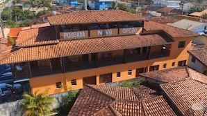 A building with a tiled roof and balconies. The building has signs that read "Pousada Nova Opção." - Pousada Nova Opção (Bertioga)