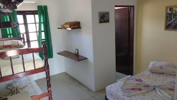 Un dormitorio con cama, una silla de madera, un estante pequeño y una puerta.