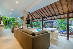A covered outdoor seating area with a sofa, chairs, and a pool.