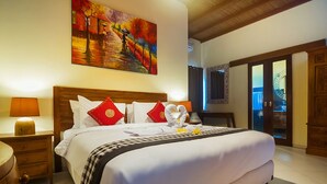 A well-lit hotel room with a large bed, a painting above the bed, and a wooden wardrobe. - Experience Mawar Estate, a 7-bedroom private villa estate in Seminyak. Accommodates up to 14 guest, includes daily breakfast, a full-time private chef, airport transfers, complimentary massages, housekeeping, and a dedicated driver. (Seminyak)