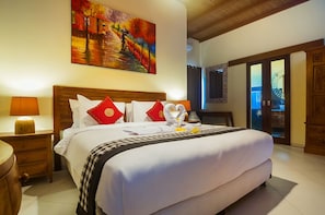 A well-lit hotel room with a large bed, a painting above the bed, and a wooden wardrobe. - Experience Mawar Estate, a 7-bedroom private villa estate in Seminyak. Accommodates up to 14 guest, includes daily breakfast, a full-time private chef, airport transfers, complimentary massages, housekeeping, and a dedicated driver. (Seminyak)