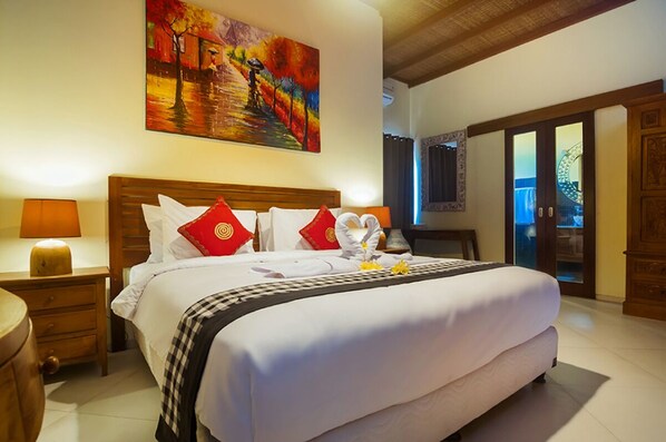 A well-lit hotel room with a large bed, a painting above the bed, and a wooden wardrobe.