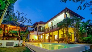 A two-story house with a swimming pool, outdoor seating, and lush greenery. - Experience Mawar Estate, a 7-bedroom private villa estate in Seminyak. Accommodates up to 14 guest, includes daily breakfast, a full-time private chef, airport transfers, complimentary massages, housekeeping, and a dedicated driver. (Seminyak)