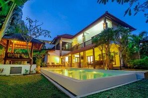 A two-story house with a swimming pool, outdoor seating, and lush greenery.