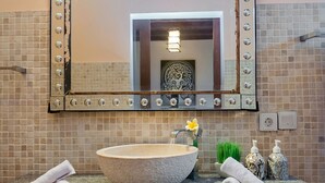 A bathroom with a large stone sink, a mirror with decorative lights, and toiletries on the counter. - Experience Mawar Estate, a 7-bedroom private villa estate in Seminyak. Accommodates up to 14 guest, includes daily breakfast, a full-time private chef, airport transfers, complimentary massages, housekeeping, and a dedicated driver. (Seminyak)