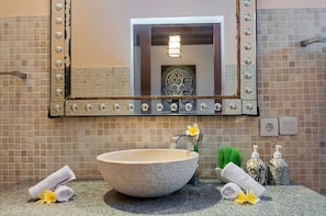 A bathroom with a large stone sink, a mirror with decorative lights, and toiletries on the counter. - Experience Mawar Estate, a 7-bedroom private villa estate in Seminyak. Accommodates up to 14 guest, includes daily breakfast, a full-time private chef, airport transfers, complimentary massages, housekeeping, and a dedicated driver. (Seminyak)