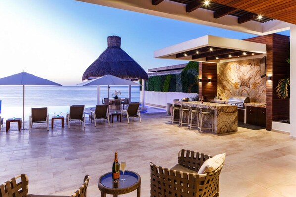 An outdoor bar area with a view of the ocean, a thatched umbrella, and seating arrangements.