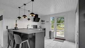 Eine moderne Küche mit einer zentralen Kochinsel, Barhocker, Pendelleuchten und Blick durch die Glastür.