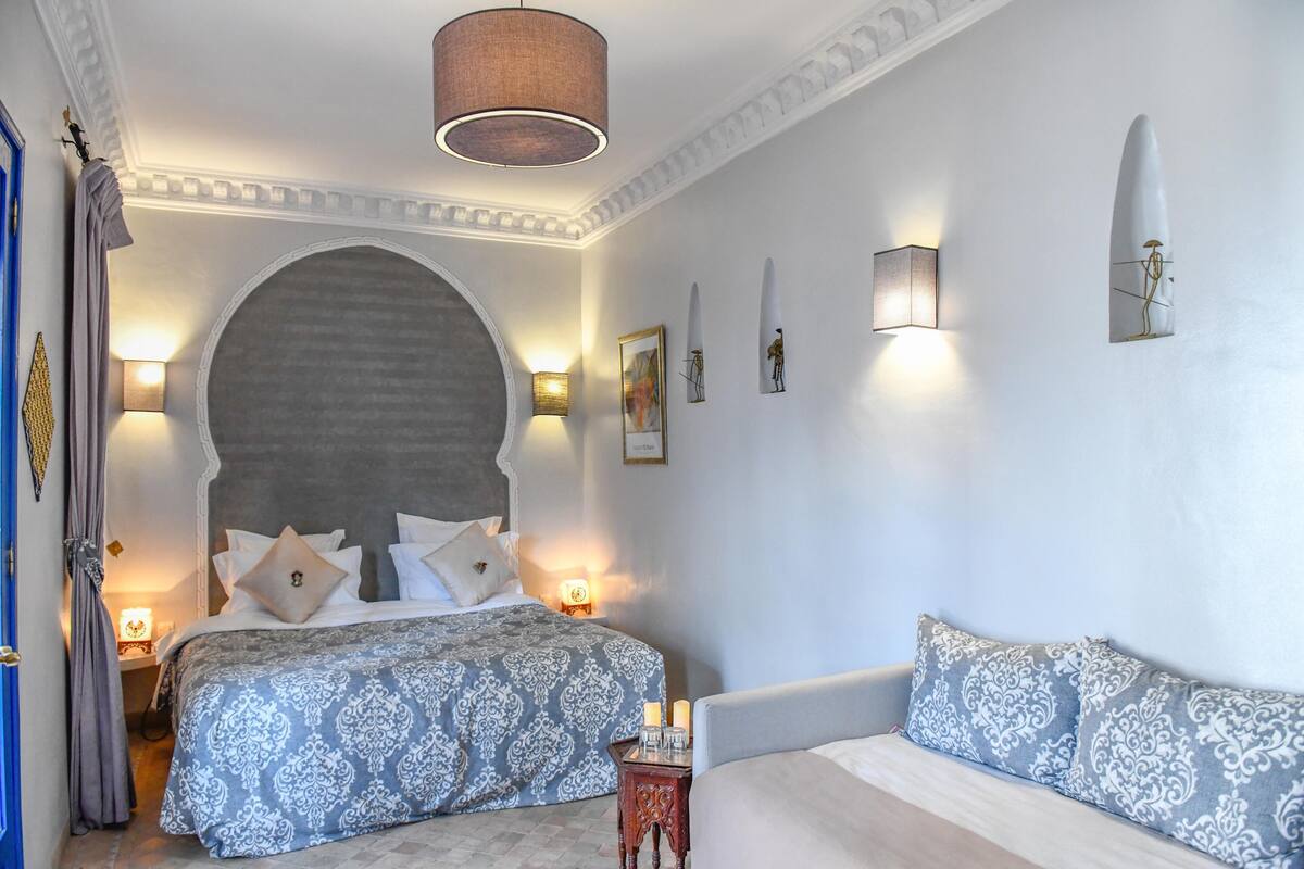 A bedroom with a large bed, two bedside tables with lamps, a sofa, and a decorative archway.