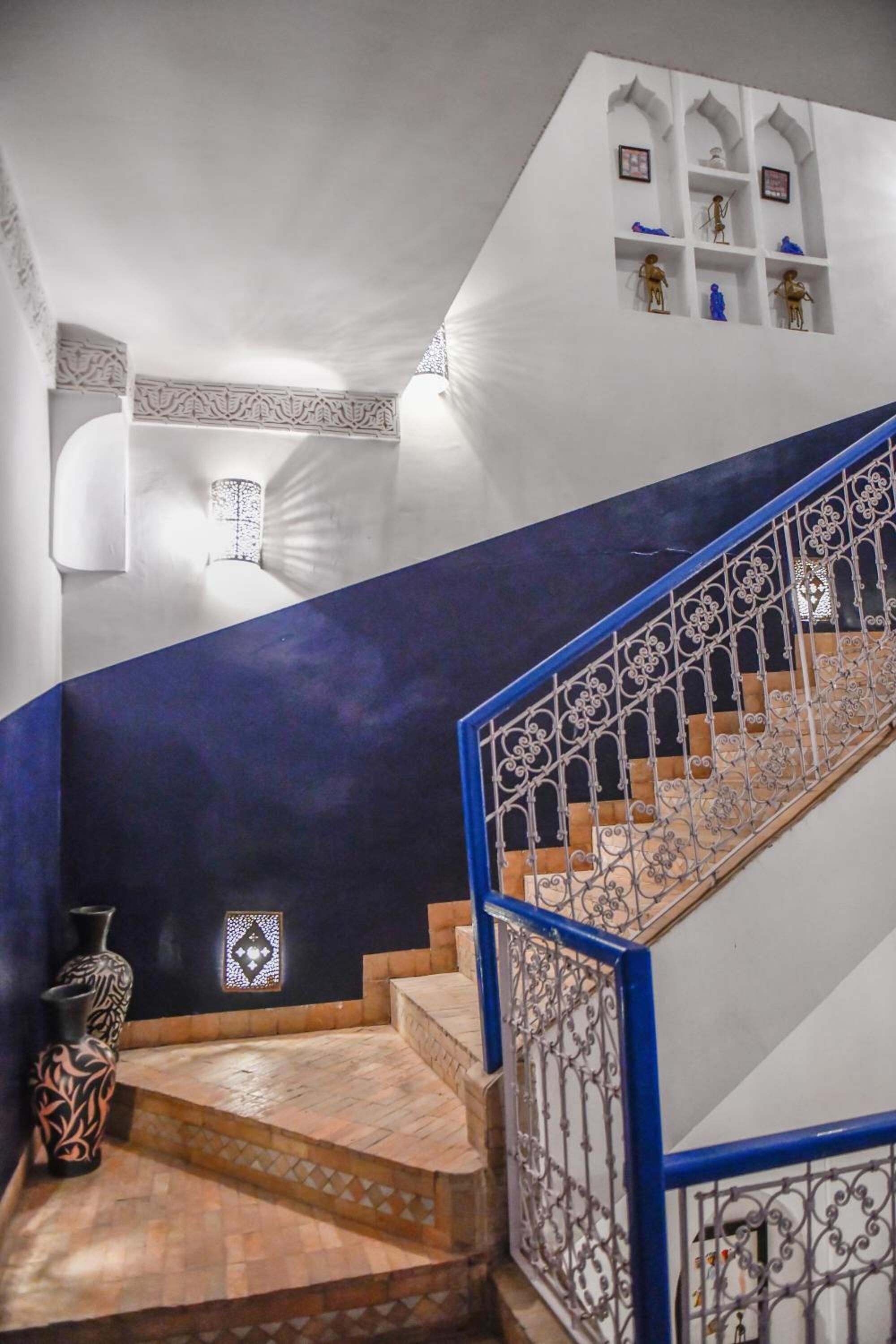 A staircase with blue railings and a patterned floor leading to a landing with decorative wall shelves.