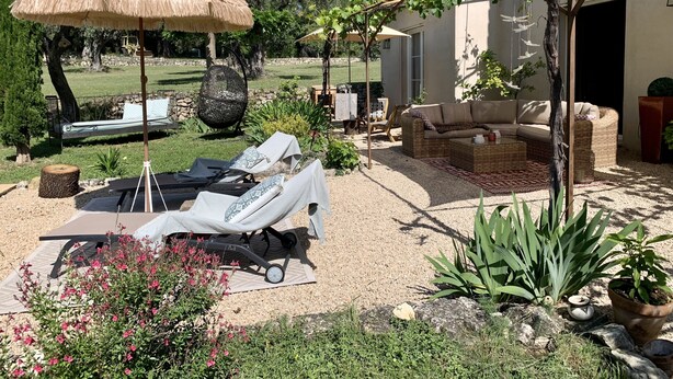 Un patio al aire libre soleado con sillones de descanso, una pérgola y una zona de estar cubierta.