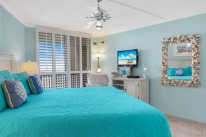 Un dormitorio con una cama grande, un ventilador de techo, un televisor y un espejo decorativo.