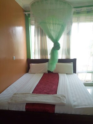 Uma cama com lençóis brancos, um cobre-cama vermelho e um dossel verde.
