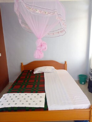 Una cama individual con cabecera de madera, una mosquitera rosa y una cesta de ropa verde.