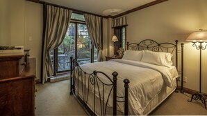A bedroom with a large window, a bed with a headboard, a bedside table with a lamp, and a dresser. - Bondurant by Tremblant Platinum (Mont-Tremblant)