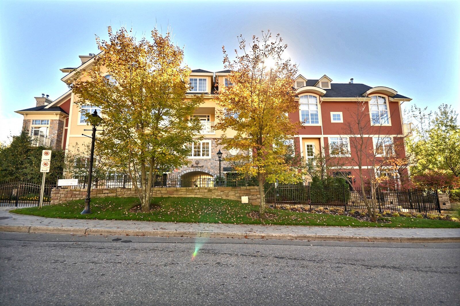 A multi-story residential building with a stone facade, large windows, and a well-maintained lawn.