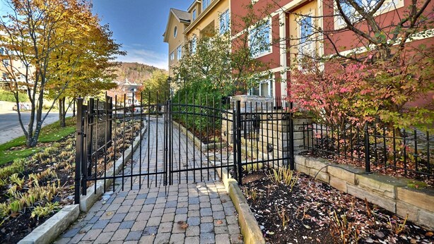 A gated entrance to a building with a paved pathway, surrounded by trees and a stone wall. - Bondurant by Tremblant Platinum (Mont-Tremblant)