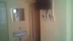 A small bathroom with a sink, mirror, and a television mounted on the wall. - Maleck Guest Rooms (Ruiru)
