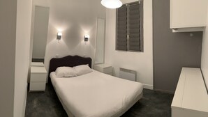 A bedroom with a bed, bedside tables, a mirror, a radiator, and a wardrobe.