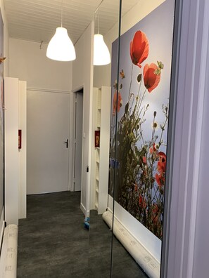 Um corredor com um grande mural floral, luminárias pendentes brancas e uma porta no final.