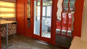 A room with a red wall, a table with chairs, a mirror, and a door leading to another room.